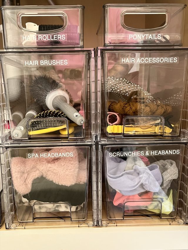 Stacked clear bins labeled hair rollers, ponytails, brushes and headbands