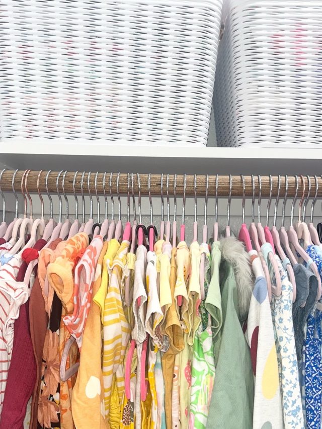 Children's clothes hung on pink hangers with woven baskets stored above