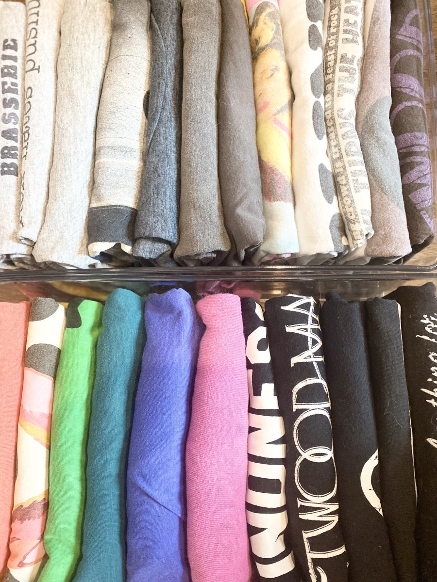 Folded sweaters and printed T-shirts stacked by color on a closet shelf