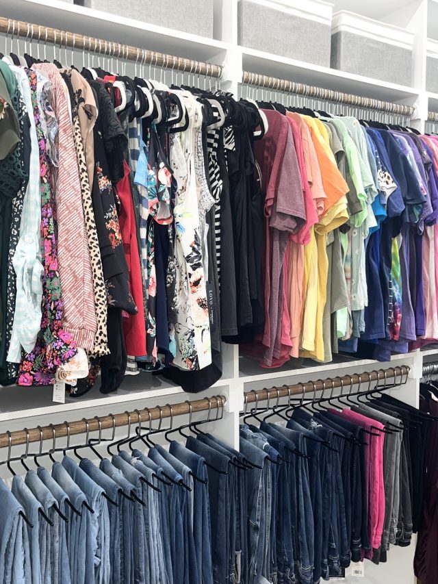 A long walk-in with printed tops above and denim hung below on wooden hangers