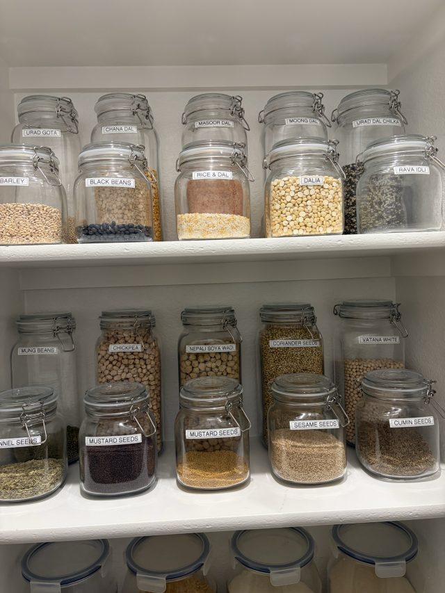 Glass jars of grains and beans labeled on the lid and shelved in rows