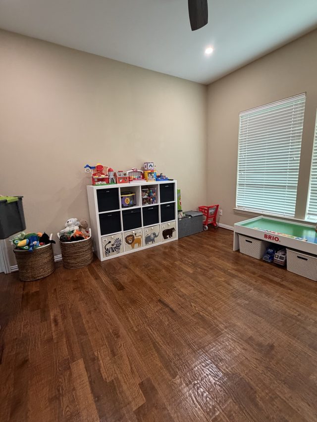 A cleared playroom with a cube shelf of toys and a train table by the window
